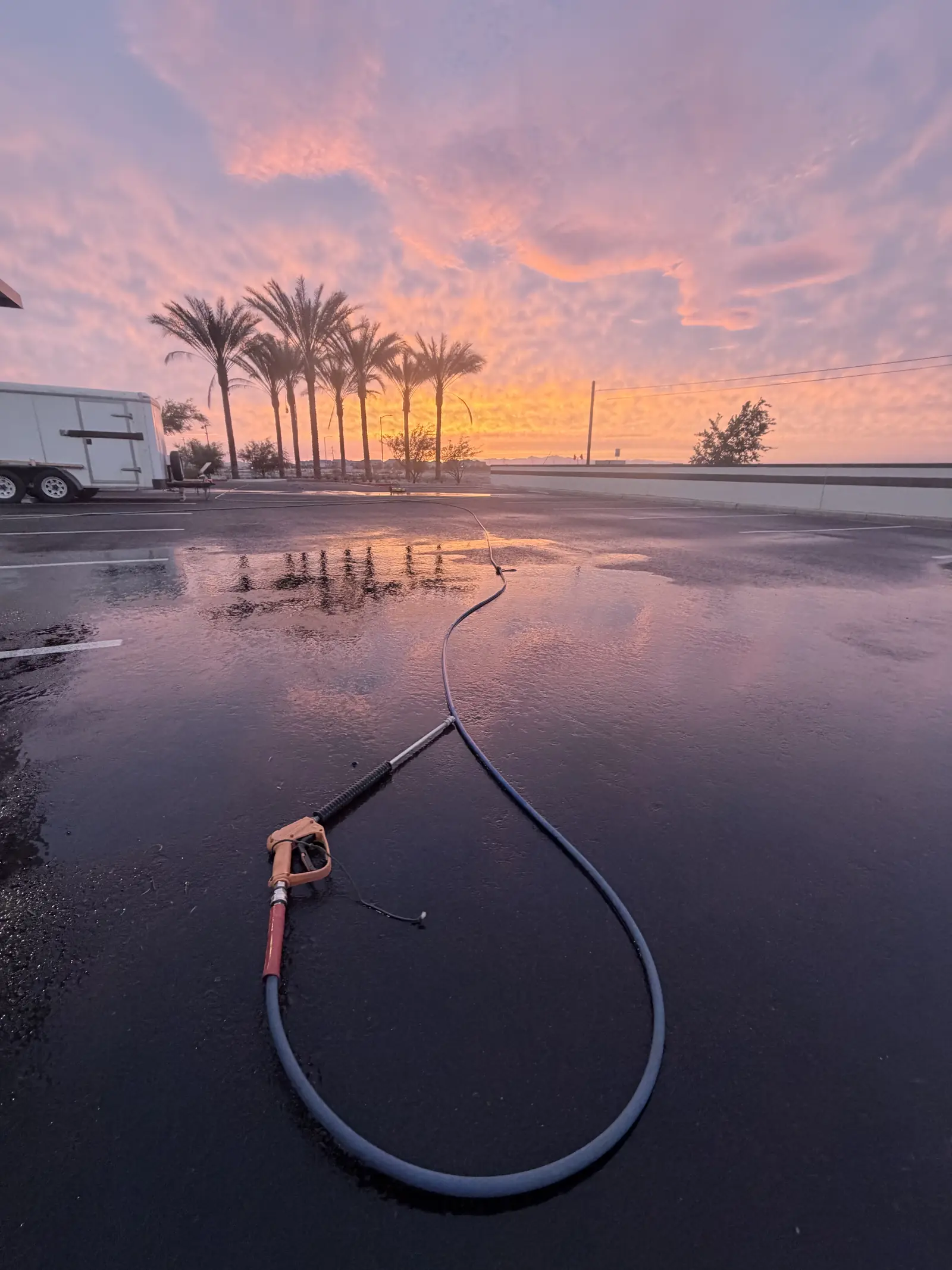 Pressure washing equipment on a wet, freshly cleaned commercial lot at sunrise